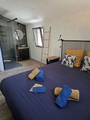 Ein modernes Hotelzimmer mit einem großen Bett, einem Badezimmer mit Duschkabine aus Glas, einer Holzleiter und Blick ins Freie.