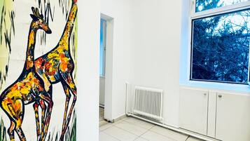 A room with white walls, a large window with a view of trees, and a painting of giraffes on the wall.
