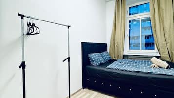 Ein Schlafzimmer mit Bett, Kleiderschrank, Fenster mit Vorhängen und einer Lampe.