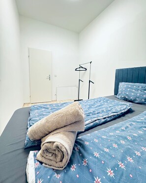 Een slaapkamer met een bed, kussens en een opgevouwen handdoek.