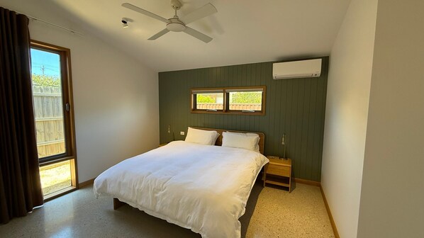 Une chambre à coucher avec un lit, une table de chevet, un ventilateur de plafond et une fenêtre.