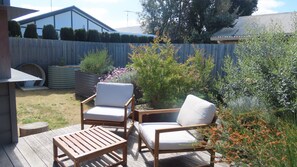 Une terrasse en bois avec deux chaises blanches dotées de coussins et une petite table.