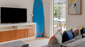 Un salon avec un téléviseur à écran plat, une planche de surf bleue et un tableau représentant un oiseau.