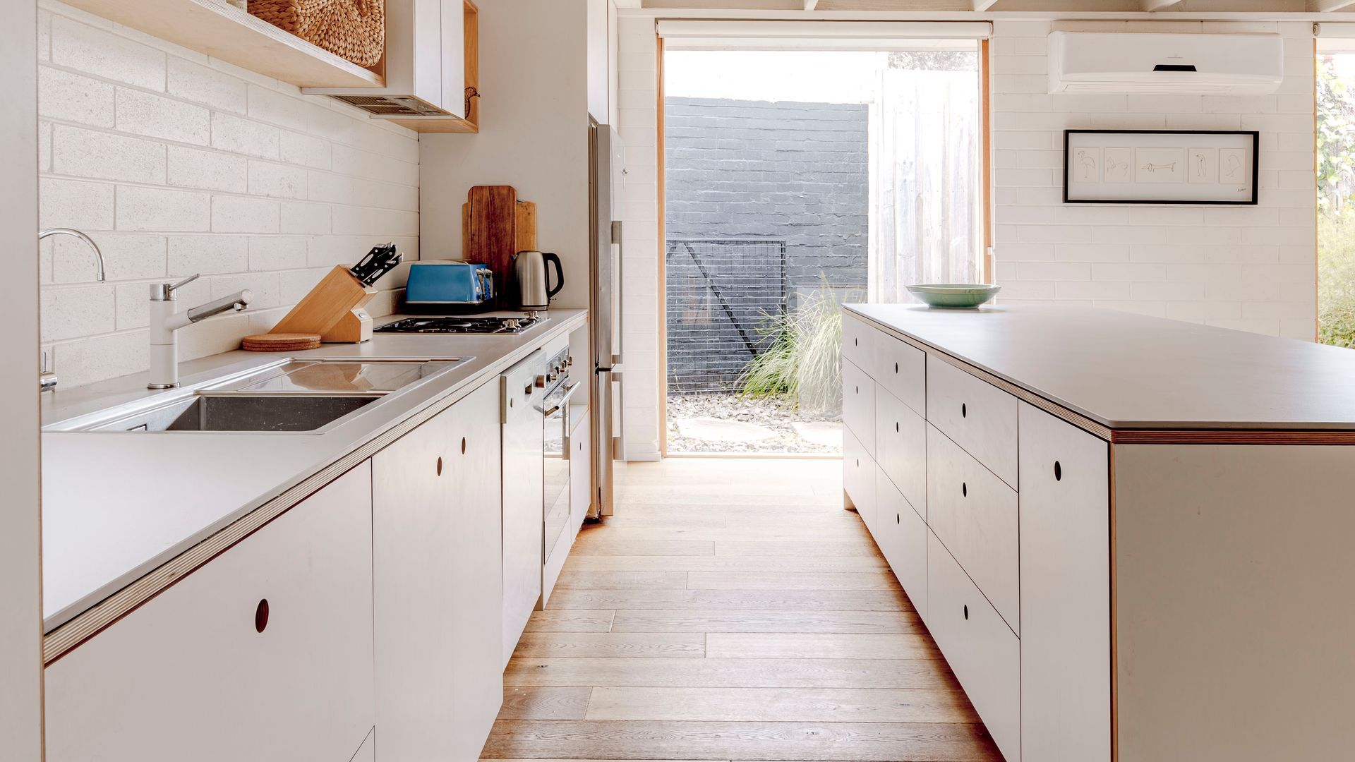 Une cuisine avec des meubles blancs, un plancher en bois et une vue sur l’extérieur.