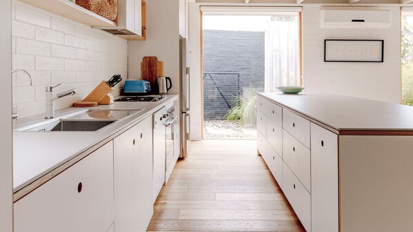 Une cuisine avec des meubles blancs, un plancher en bois et une vue sur l’extérieur.