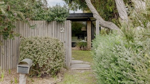 Una puerta de madera con el número 2, un buzón y un sendero que lleva a una zona exterior cubierta con un banco.