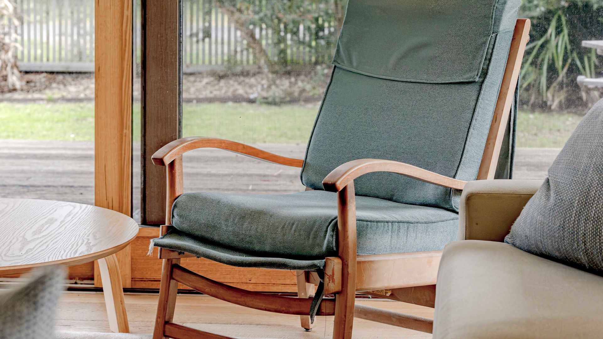 Une chaise en bois dotée d’un siège et d’un dossier rembourrés, placée près d’une fenêtre donnant sur un jardin.