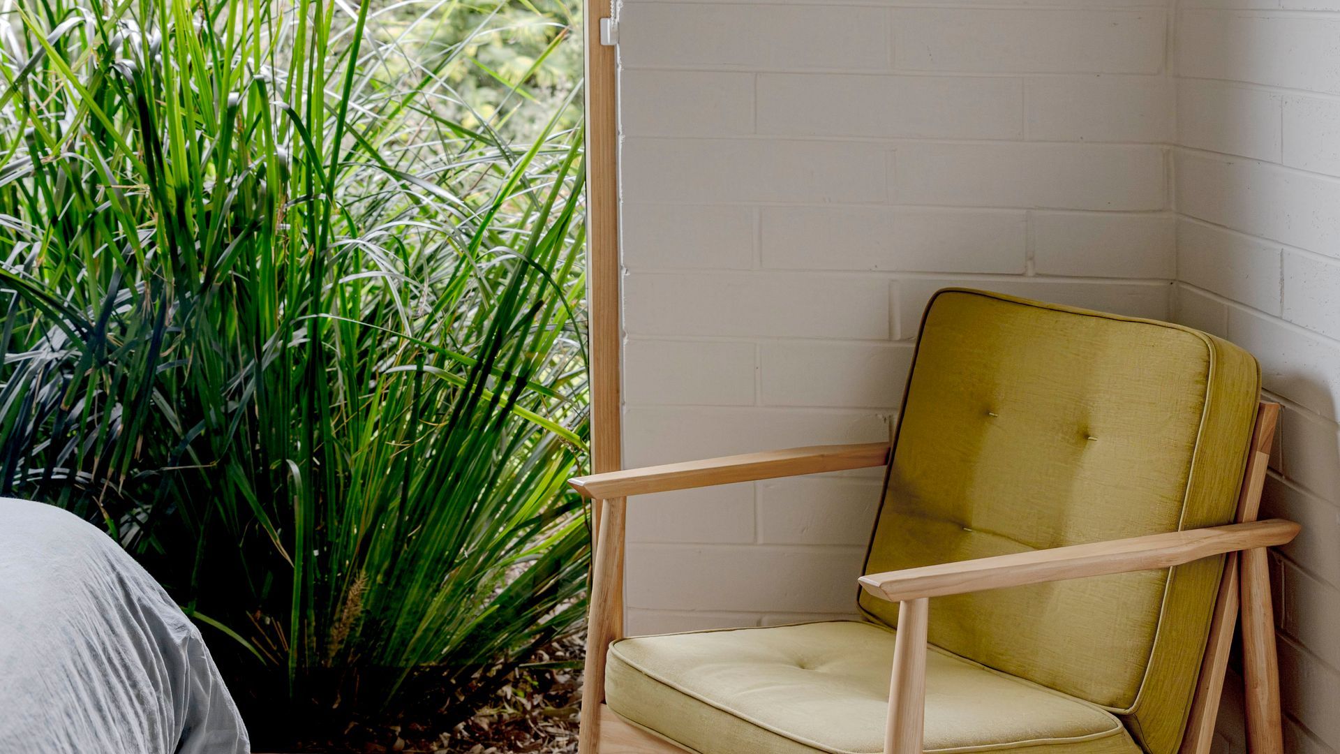 Un coin de pièce avec un fauteuil jaune recouvert de tissu et un mur en briques blanches.