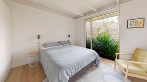 Un dormitorio con una cama grande, una silla, un escritorio y una ventana con vistas a zonas verdes.