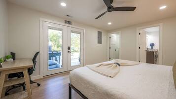 A bedroom with a bed, a desk, and a chair. There is a door leading to a balcony.