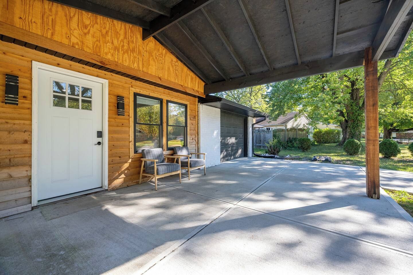A covered porch with a wooden exterior, a white door, and two chairs.