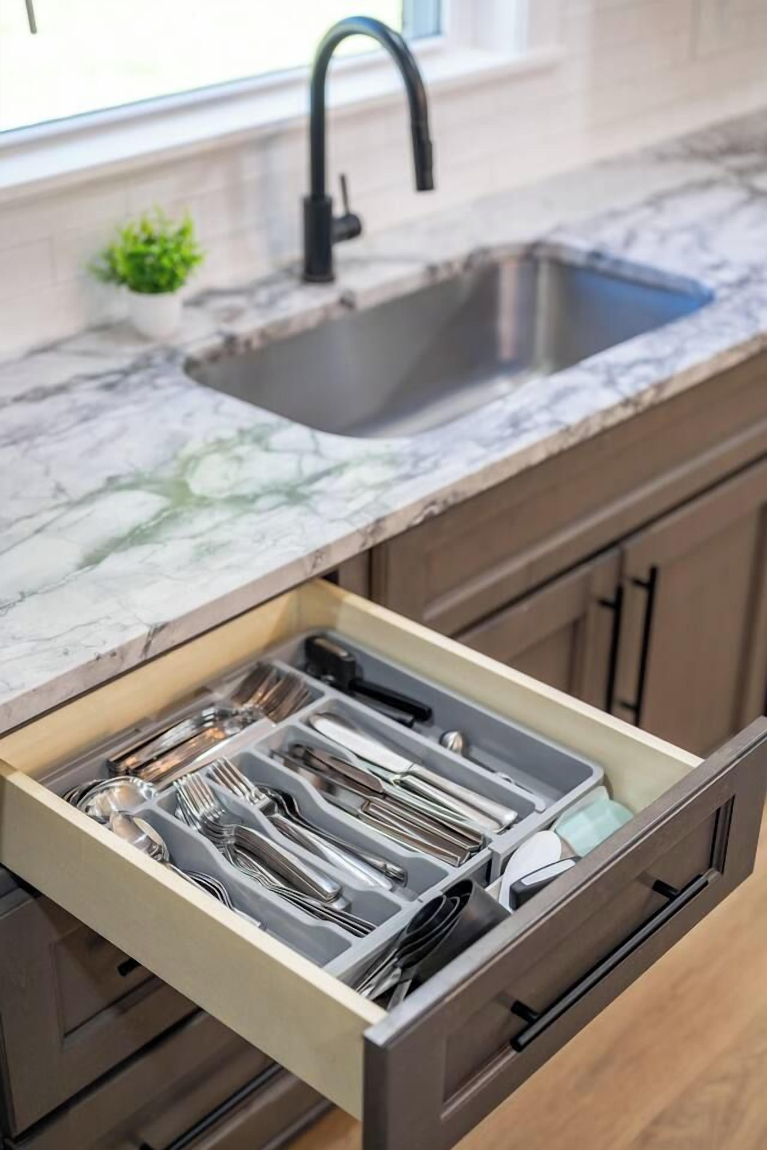 A kitchen with a marble countertop, a sink, and a drawer with utensils.