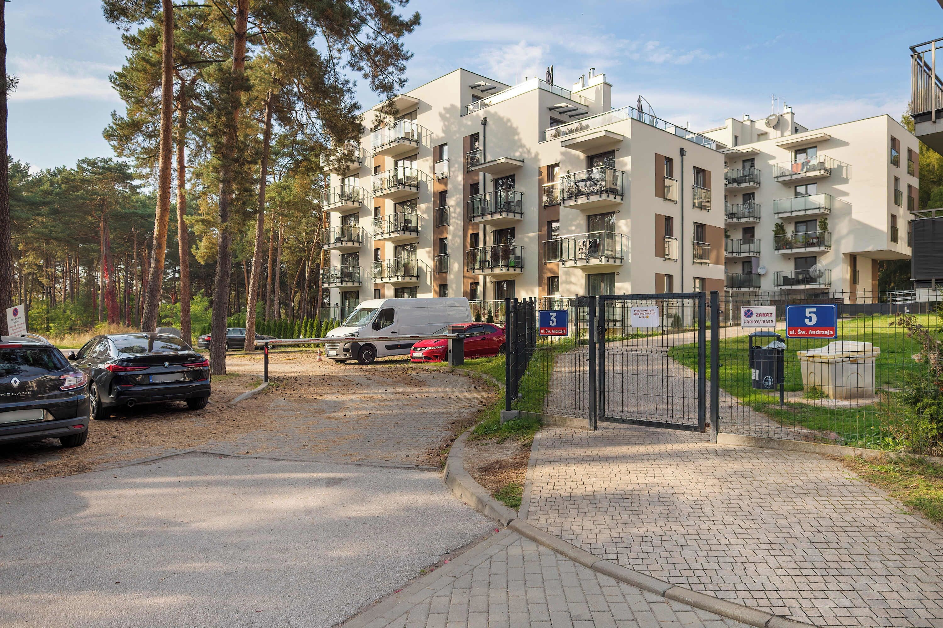 Ein mehrstöckiges Wohngebäude mit Balkonen, einem Parkplatz mit Autos und einem befestigten Eingangsbereich.