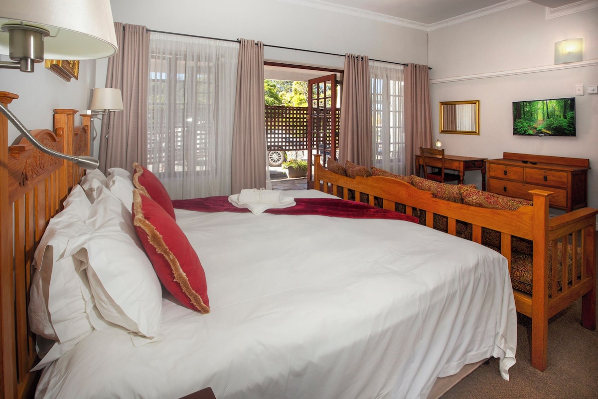 A hotel room with a large bed, a desk, a chair, a television, and a window with curtains.