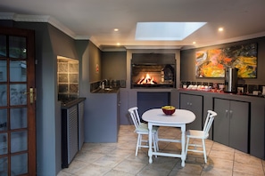 A kitchen with a built-in fireplace, a dining table with chairs, and a painting on the wall. - Sir Roys Guest House (Gqeberha)