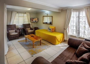 A hotel room with a bed, two armchairs, a sofa, a wooden table, and a TV. - Sir Roys Guest House (Gqeberha)