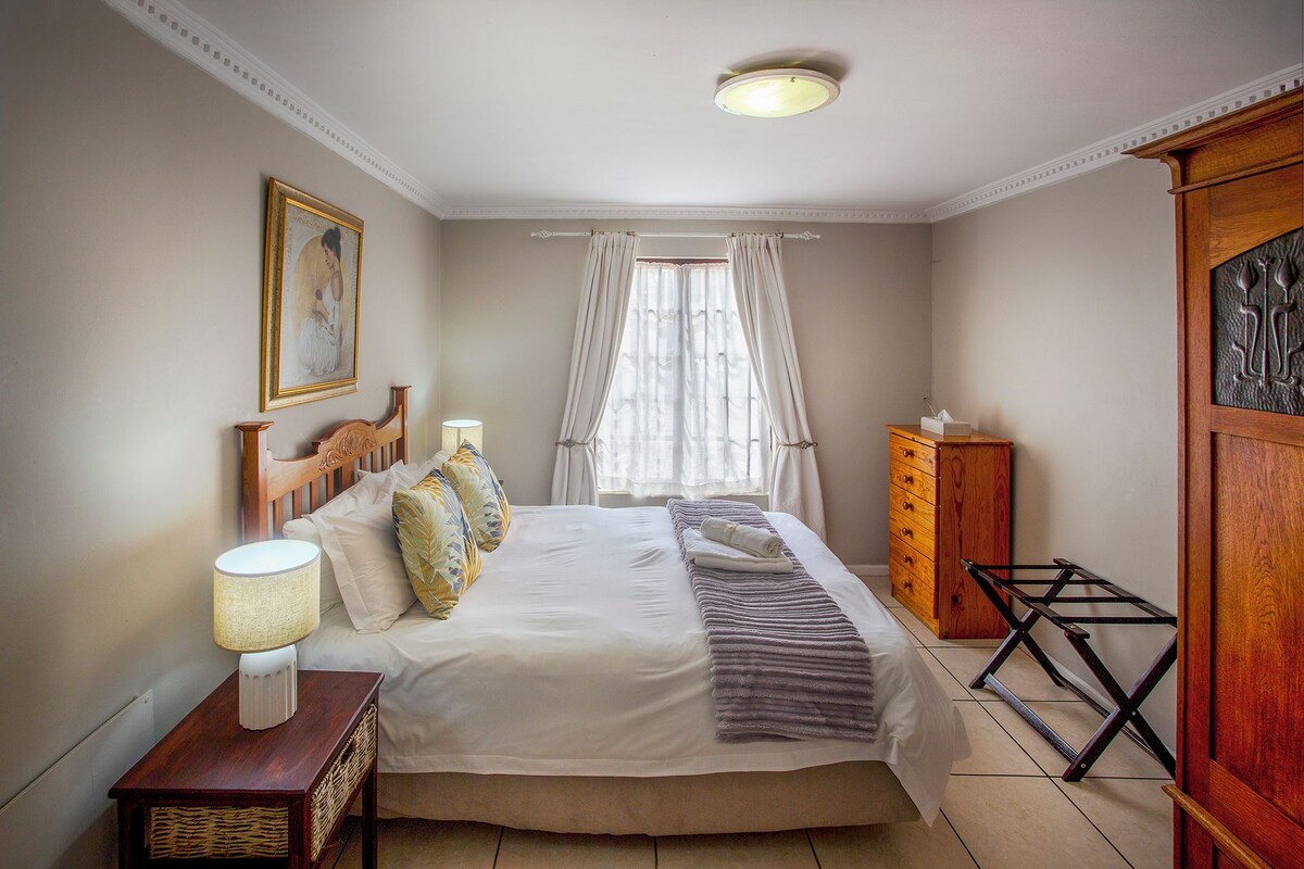A neatly arranged bedroom with a bed, bedside lamps, a dresser, and a window with curtains.
