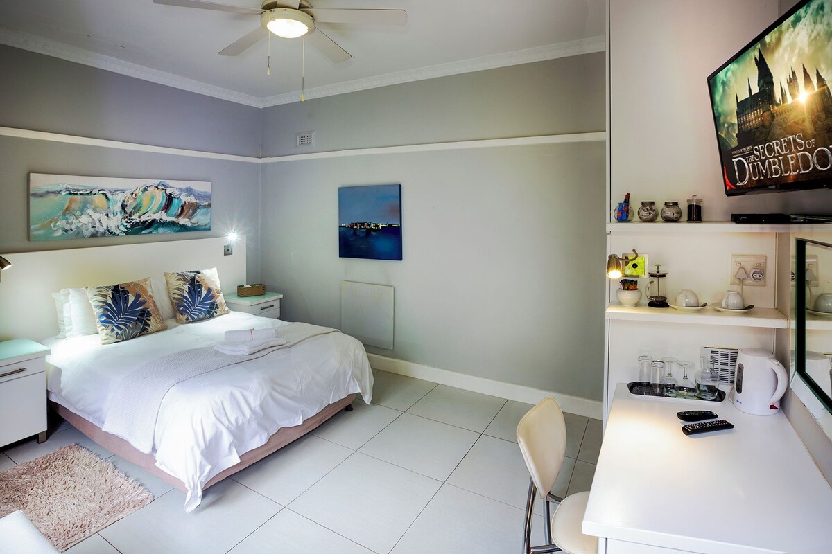 A hotel room with a bed, bedside table, lamp, artwork, and a television on a stand.
