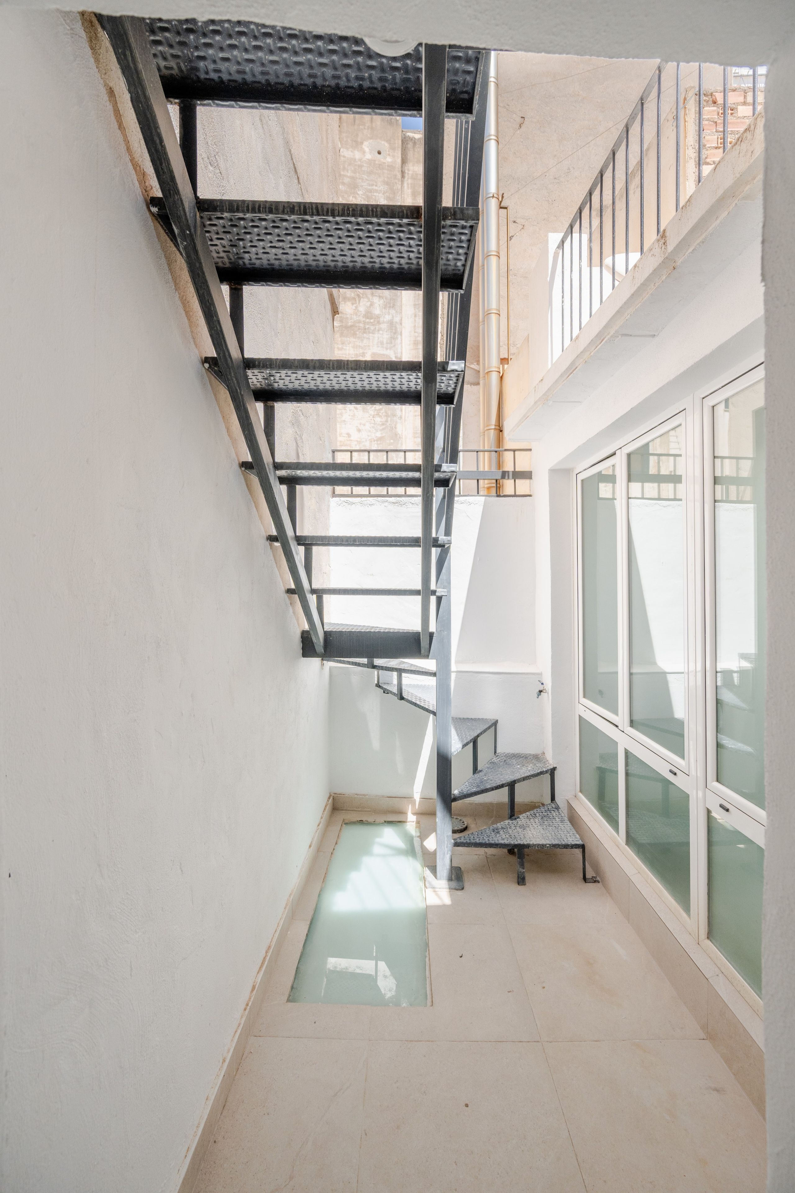 Un intérieur moderne avec un escalier en métal, une petite fenêtre et un sol carrelé.