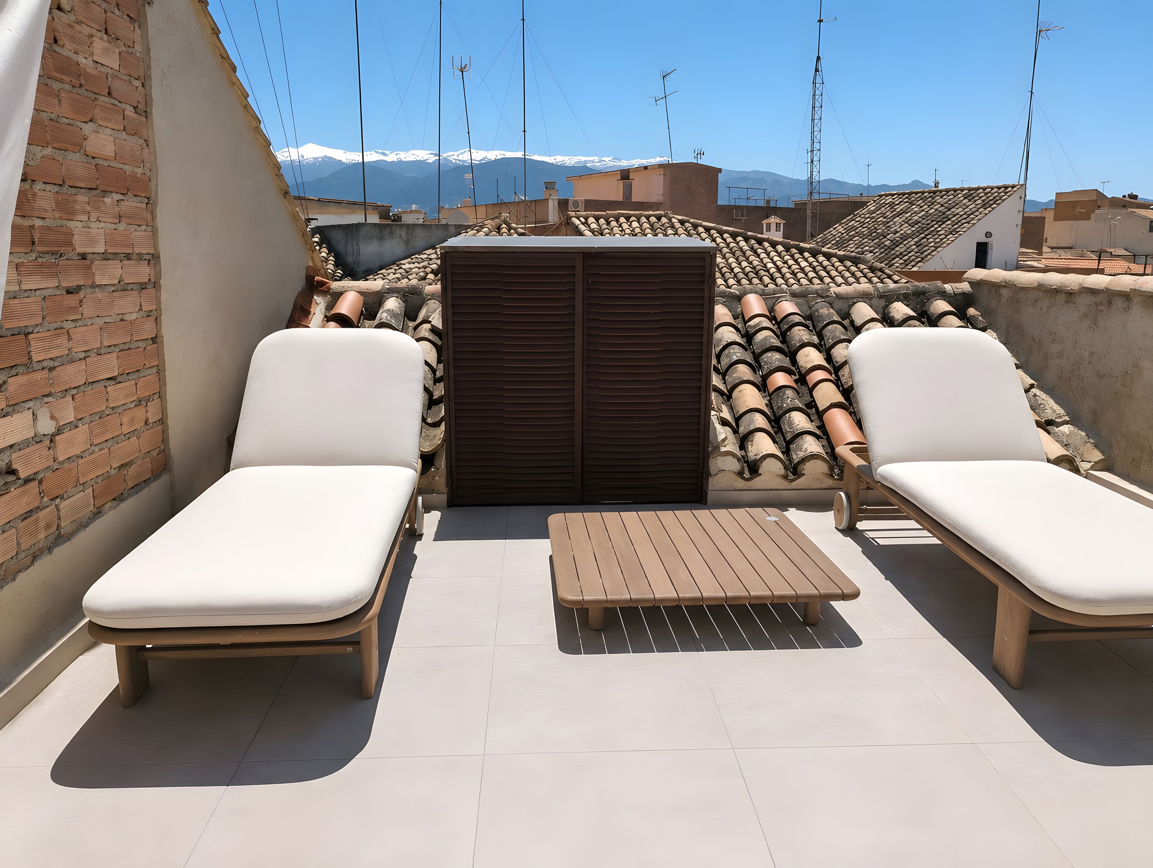 A rooftop terrace with two lounge chairs, a small table, and a brick wall.