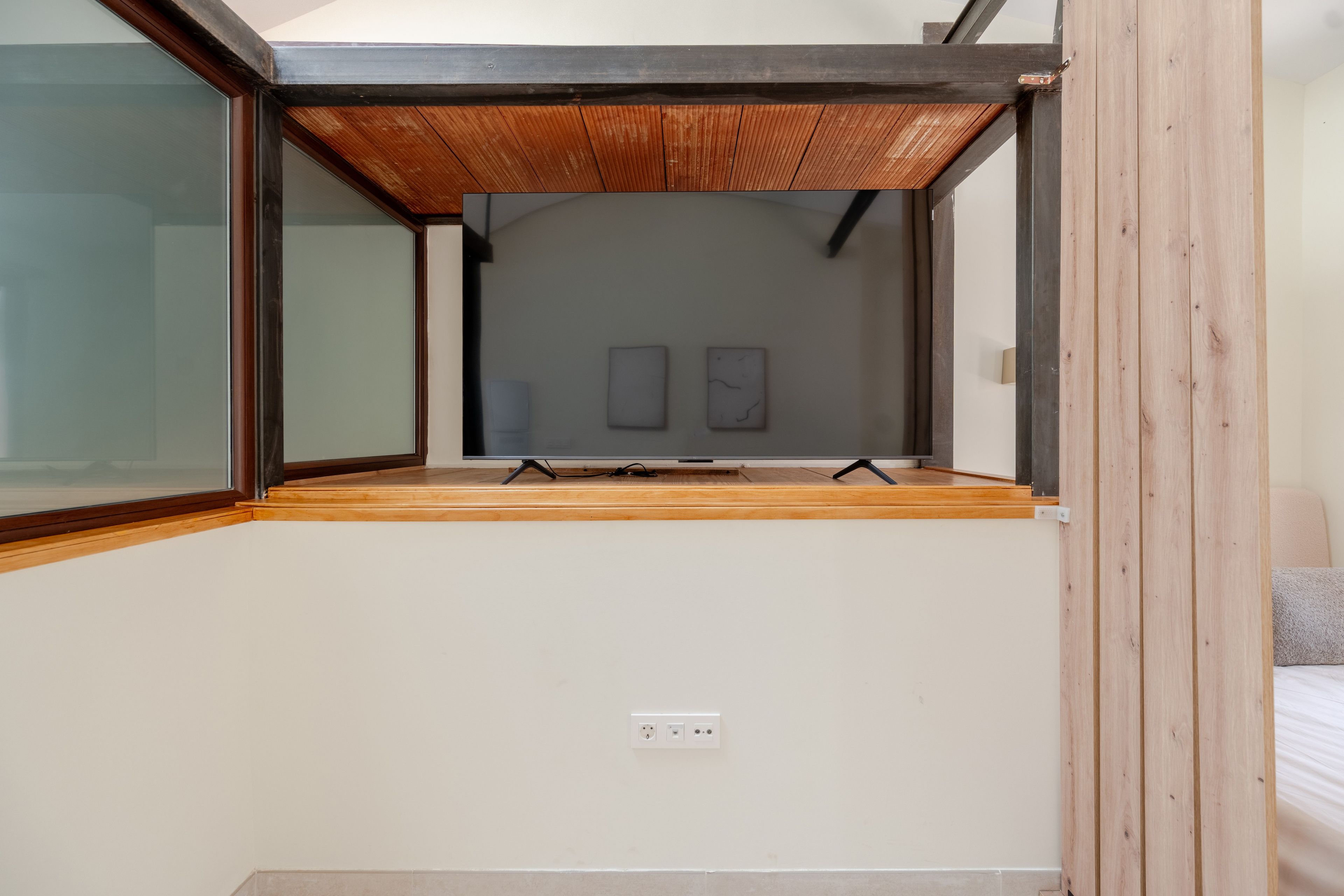 A room with a sloped ceiling, a wooden floor, and a single power outlet on the wall.