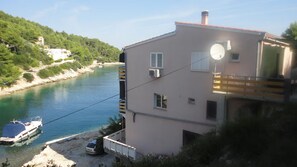 A building with a balcony overlooking a body of water, a boat docked nearby, and a hilly landscape in the background. - studio Jasna (Kukljica)