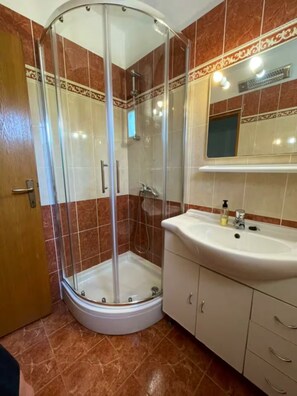 A bathroom with a glass-enclosed shower, a sink, and a mirror above it. - studio Jasna (Kukljica)