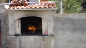 Une structure en béton dans laquelle brûle un feu, entourée d’un toit en métal et d’un mur en béton.