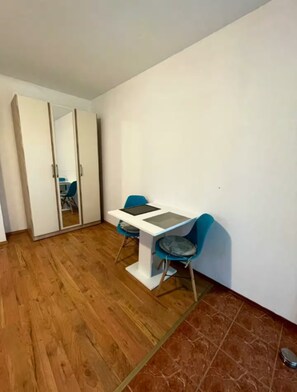 Une pièce avec un plancher en bois, une table blanche et deux chaises, ainsi qu’une armoire à portes coulissantes.