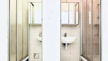 Ein modernes Badezimmer mit Duschkabine aus Glas, einem weißen Waschbecken und einem Spiegel darüber.
