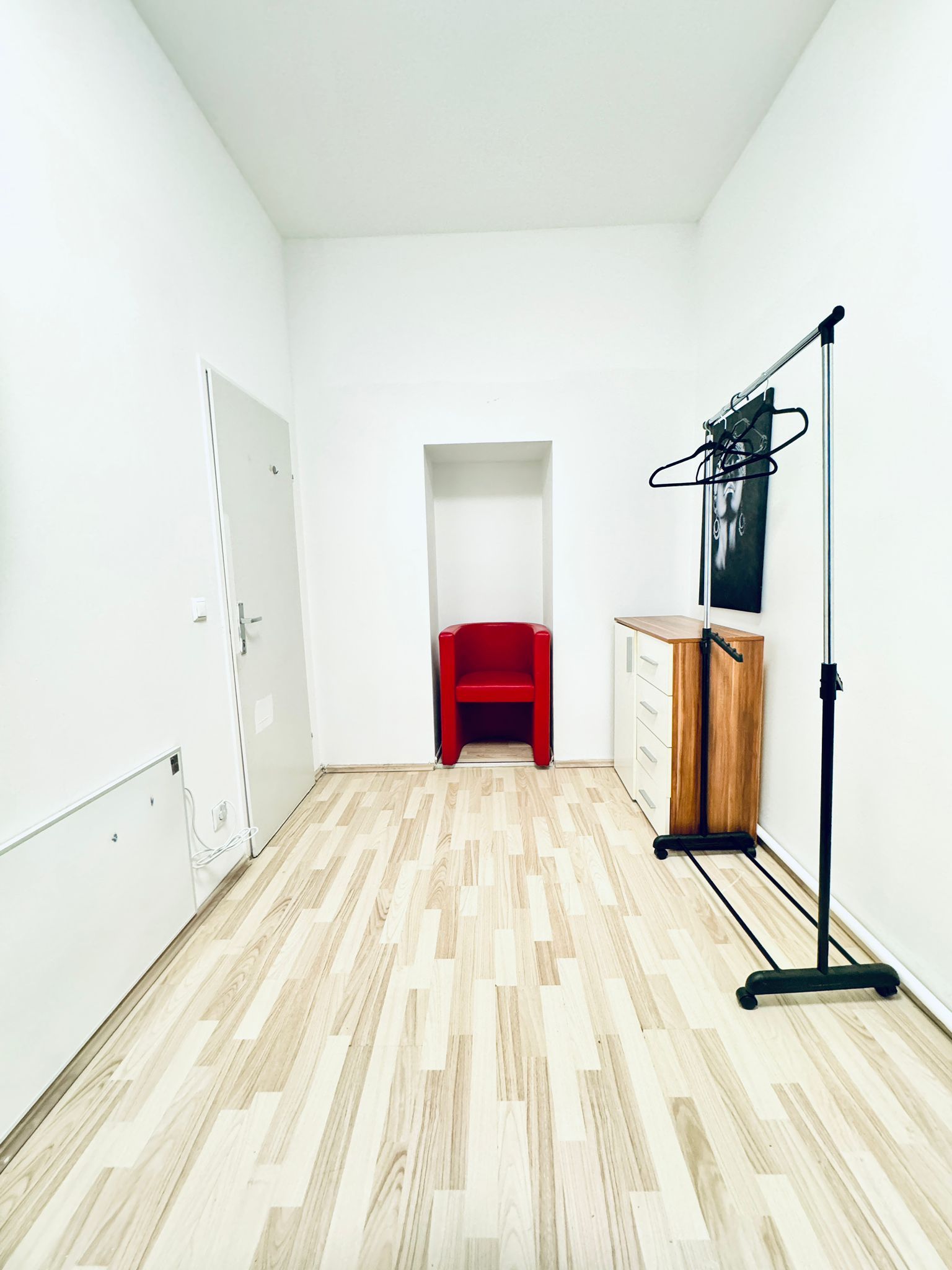 A room with a wooden parquet floor, a red chair, a wooden cabinet, and a black stand with a mirror.