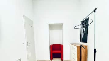 A room with a wooden parquet floor, a red chair, a wooden cabinet, and a black stand with a mirror.