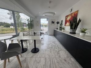 A modern interior with a dining area, kitchen, and large windows offering a view of the outdoors. - Vallentuna Hotel Apartments (Stockholms län)