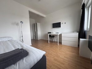 A modern hotel room with a bed, a desk, a chair, a flat-screen TV, and a wardrobe. - Vallentuna Hotel Apartments (Stockholms län)
