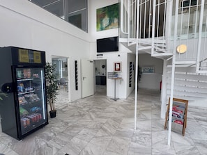 A modern lobby with a reception desk, a vending machine, a staircase, and a mural on the wall. - Vallentuna Hotel Apartments (Stockholms län)