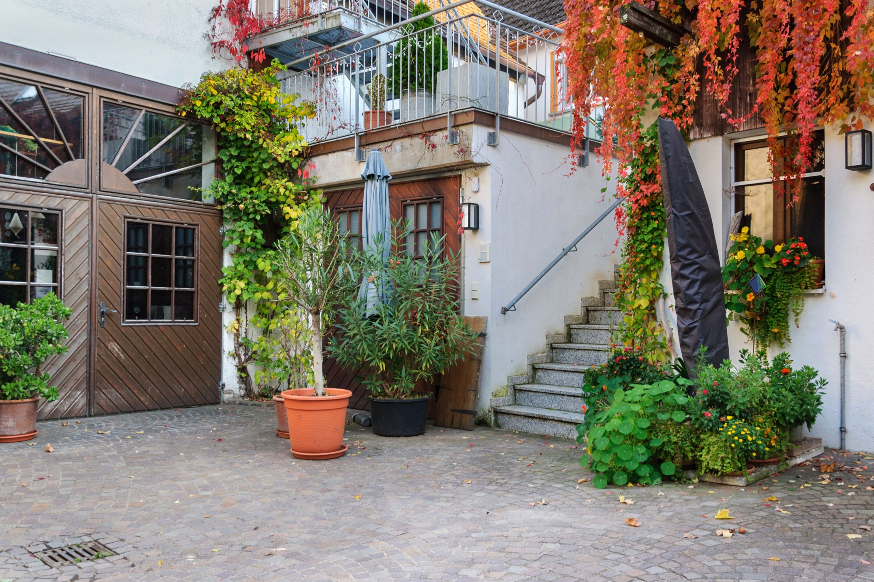 A courtyard with a wooden gate, potted plants, a staircase, and a building with a balcony.