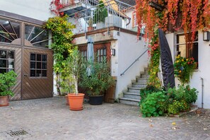 A courtyard with a wooden gate, potted plants, a staircase, and a building with a balcony.