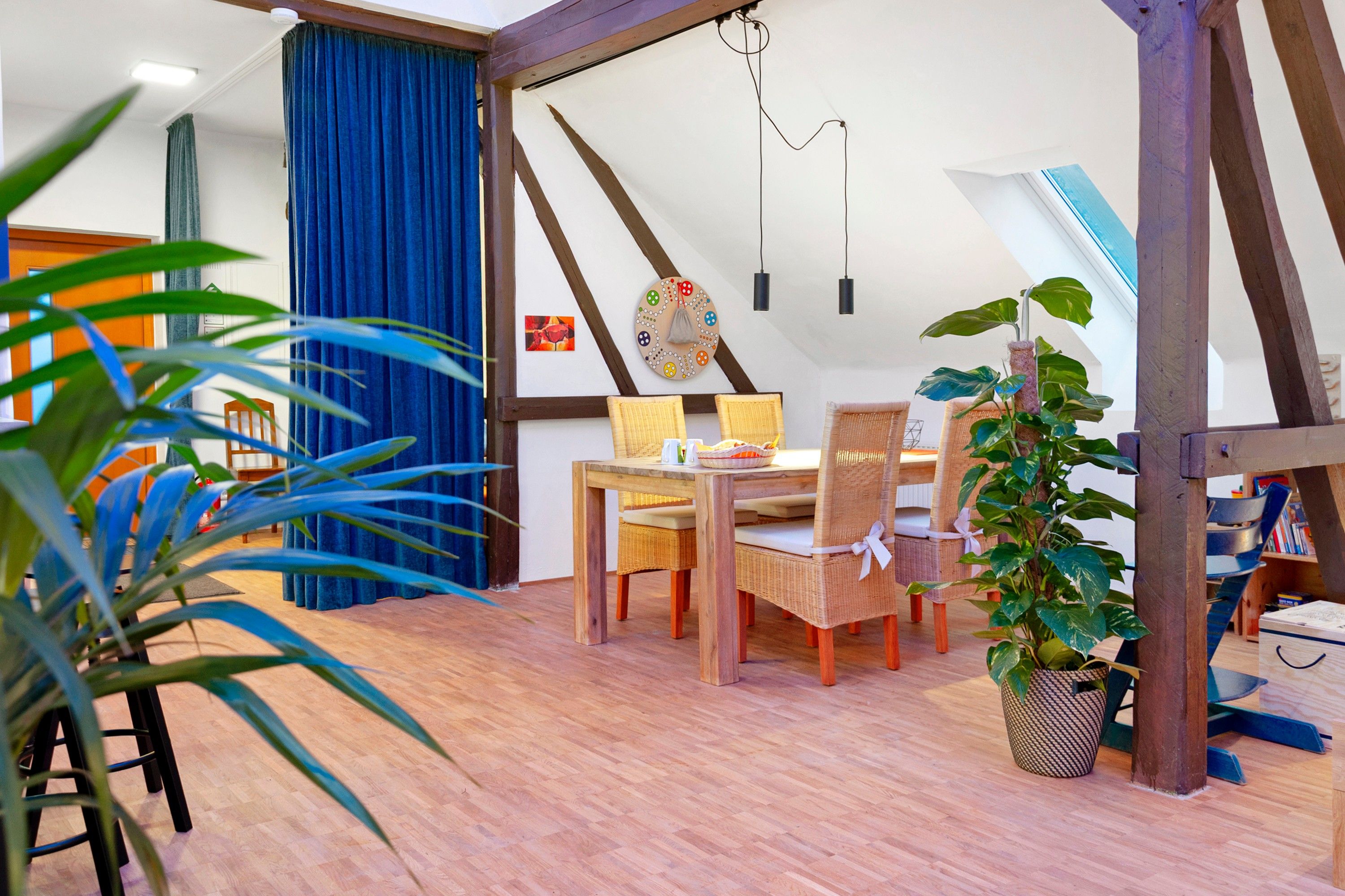 Una habitación acogedora con una mesa de comedor de madera, sillas de mimbre, una planta en maceta y una cortina azul.