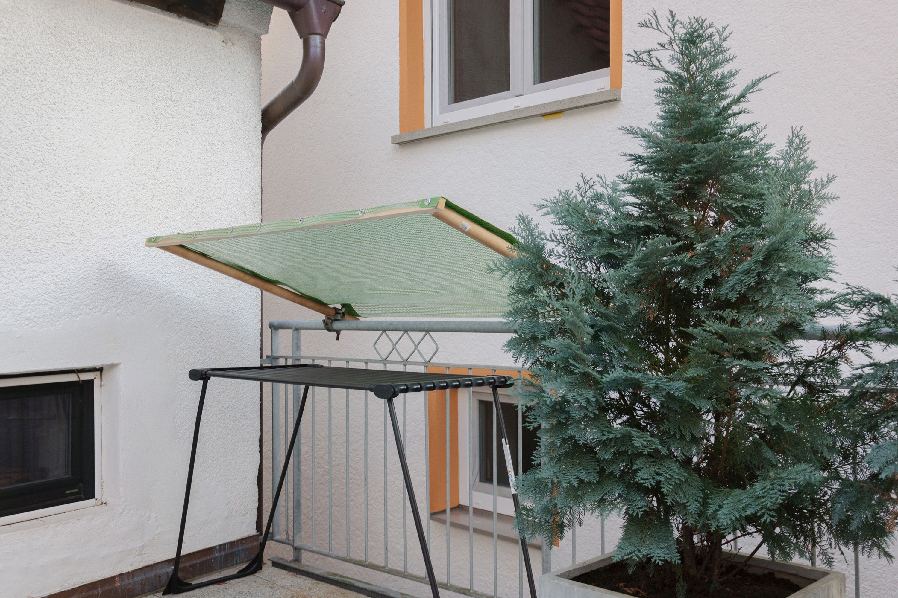 Ein Balkon mit Metallgeländer, einem grünen Markisenvorzelt und einem Topf mit immergrüner Pflanze.