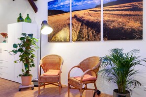 Ein Zimmer mit zwei Korbstühlen, einem Blumentopf, einem Schrank und einem großen Landschaftsbild an der Wand.