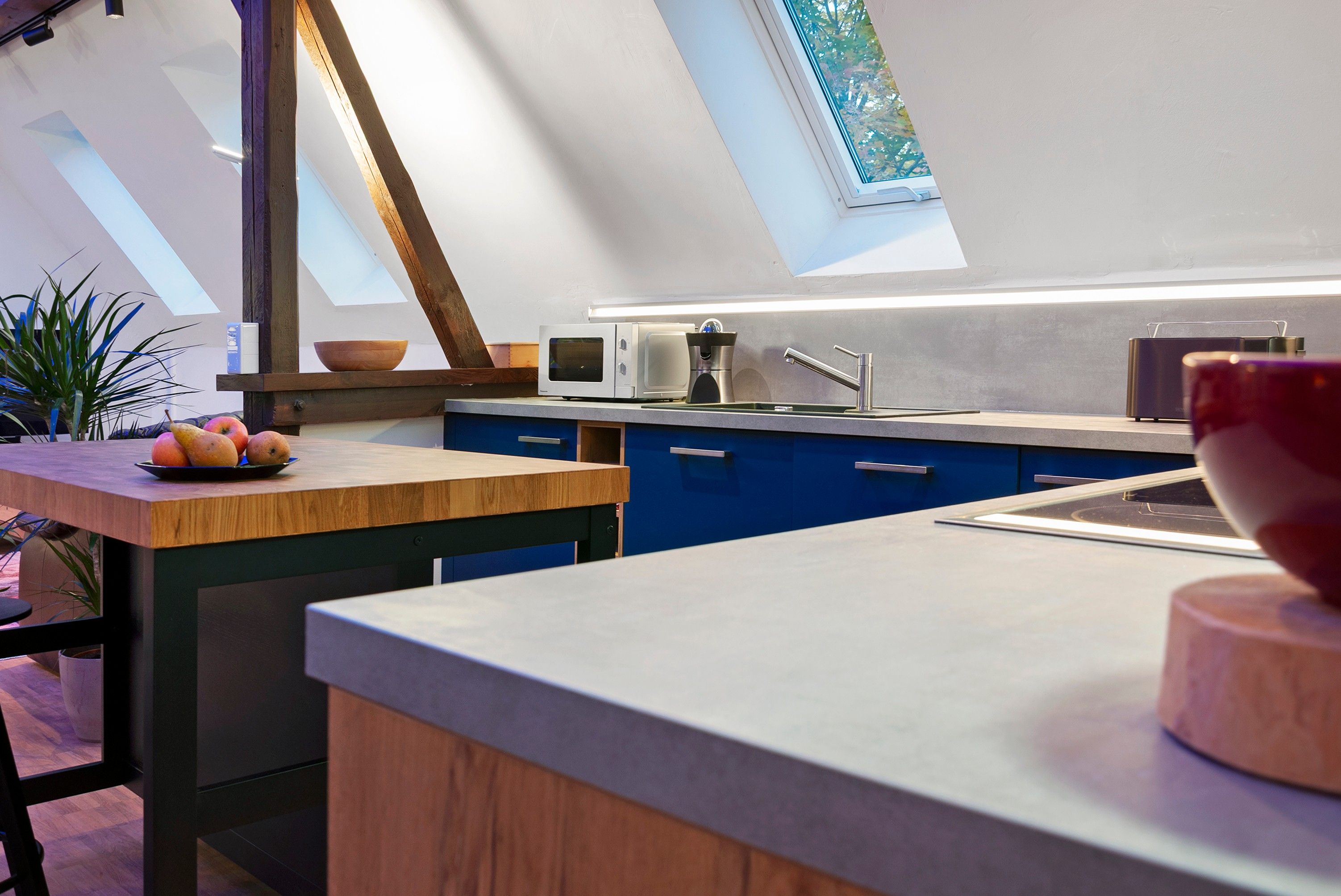 A modern kitchen with a skylight, a wooden table with fruit, and a built-in microwave.