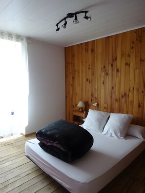 Habitació d'hotel amb paret de panells de fusta, un llit amb roba de llit blanca, un coixí negre i una taula de nit amb una làmpada.