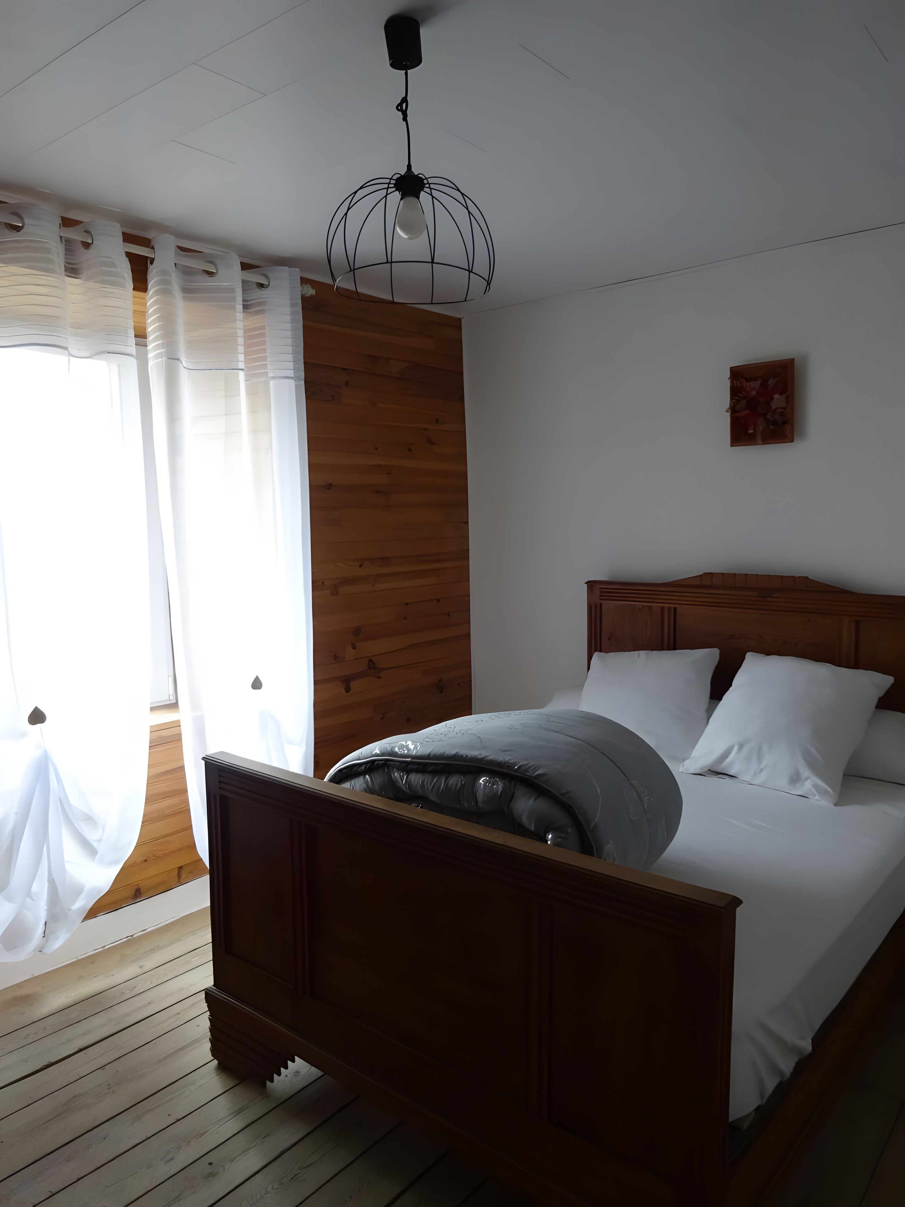 Un dormitorio con cama de madera, ropa de cama blanca, cabecera de madera, lámpara de techo y panel de pared de madera.