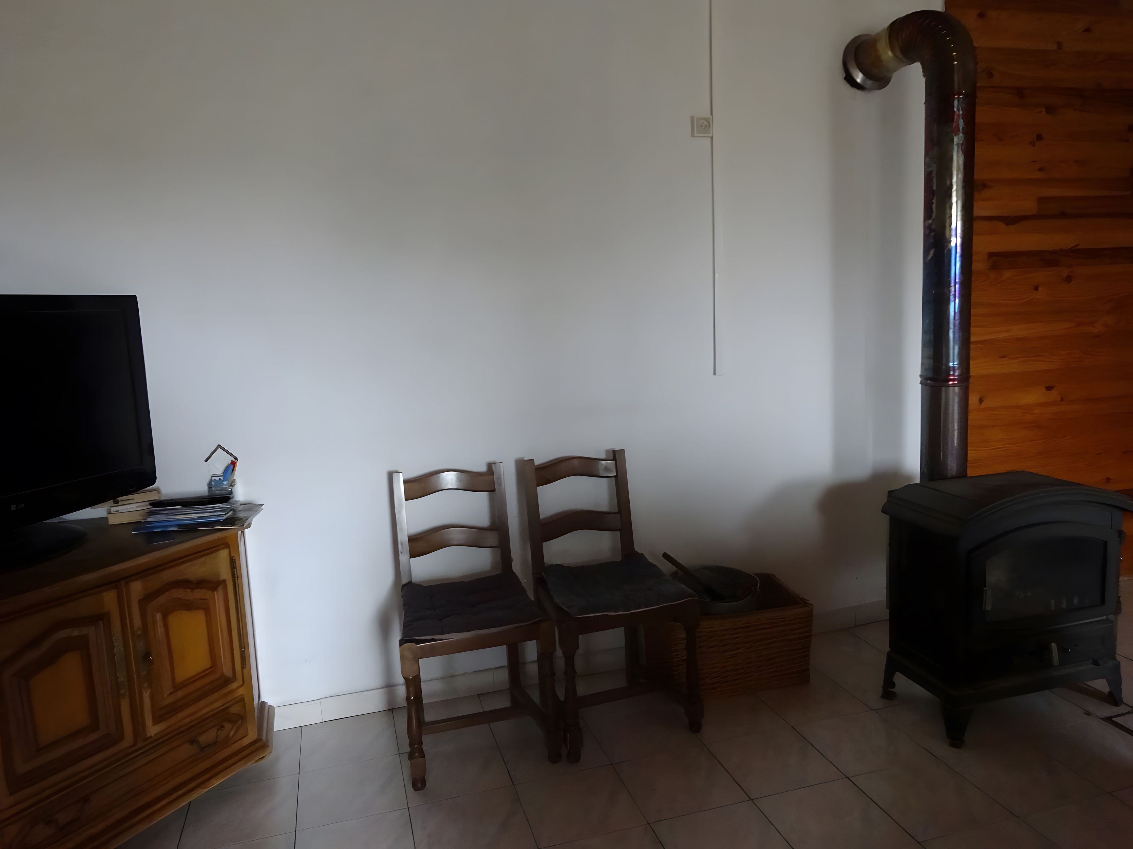 Een kamer met een televisie op een houten kast, twee houten stoelen, een open haard en een betegelde vloer.