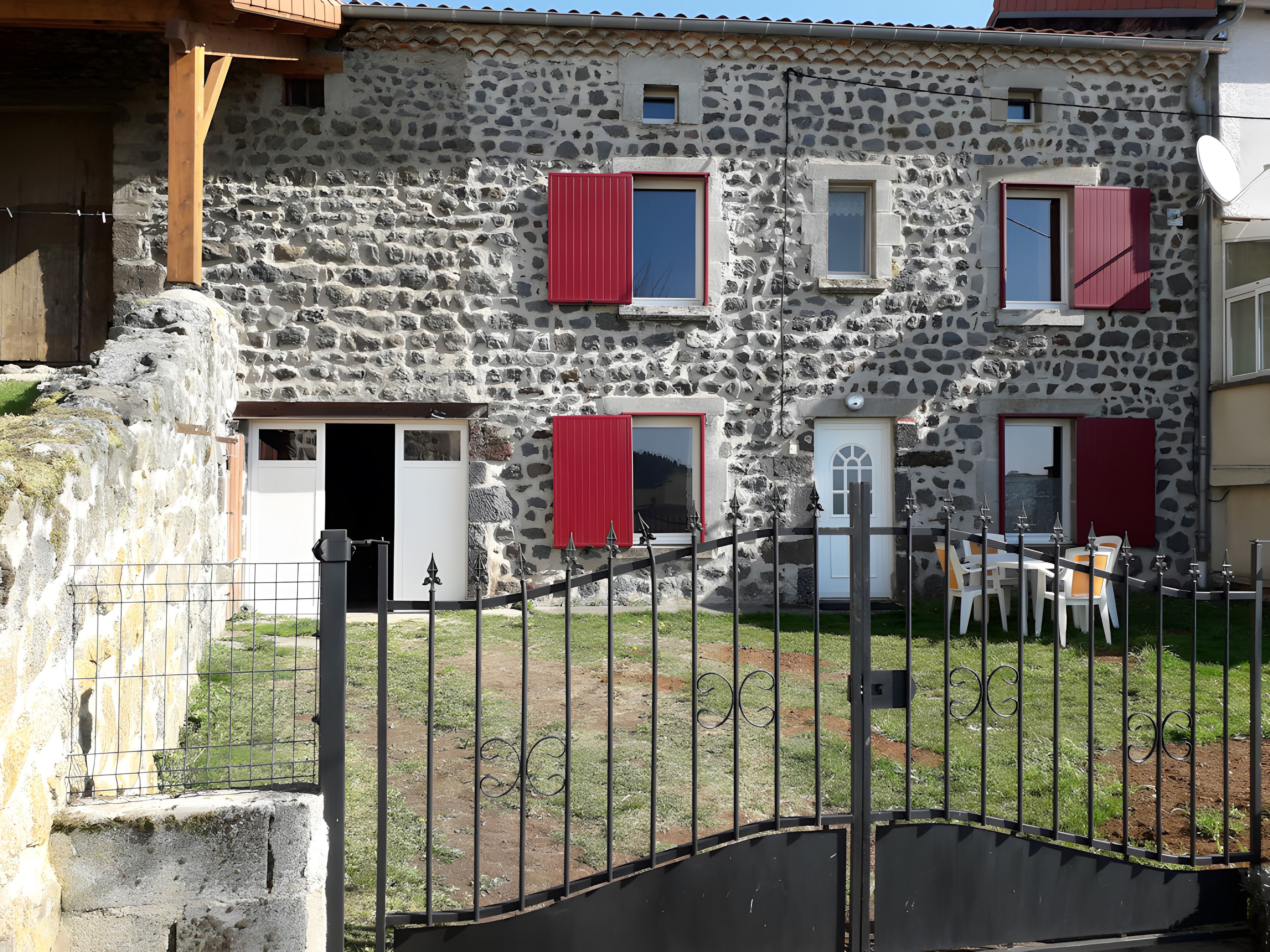 Un bâtiment en pierre doté de nombreuses fenêtres et portes, une entrée fermée par un portail et un petit espace extérieur aménagé avec des sièges.