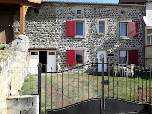 Edifici de pedra amb diverses finestres i portes, entrada amb reixa i una petita zona d'seure a l'exterior.