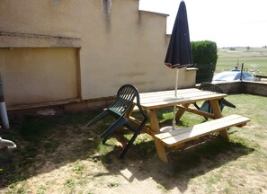 An outdoor patio with a wooden table and chairs, a bench, and a black umbrella. - House on the Chemin de Régordane (Landos)