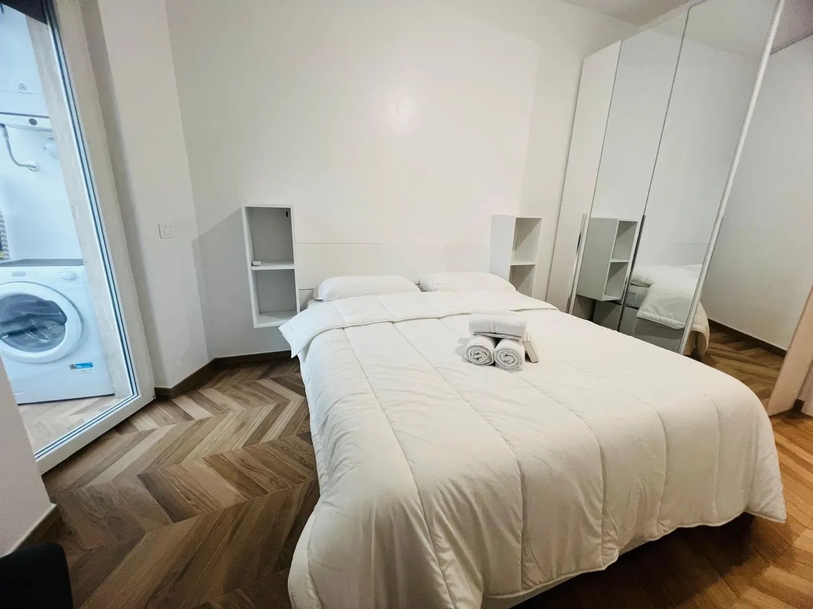 A hotel room with a bed, a washing machine, and a mirror.