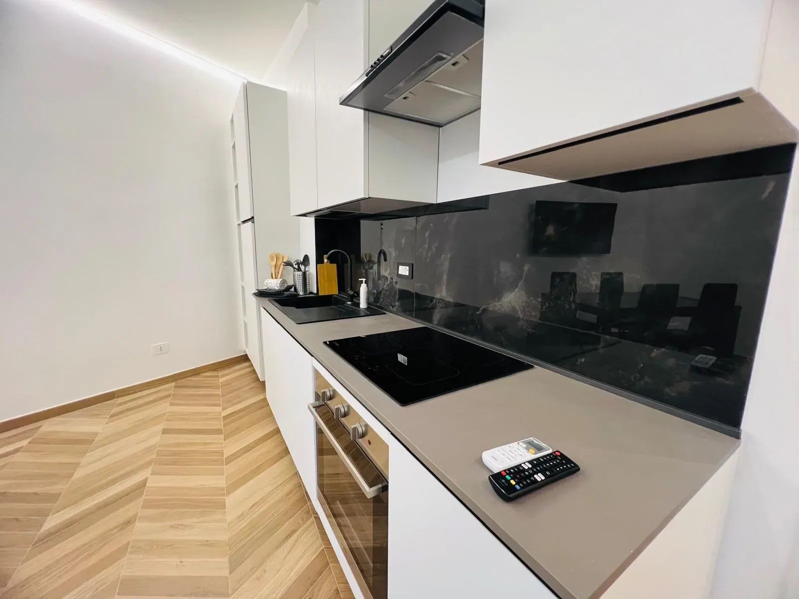 A modern kitchen with a black induction cooktop, a stainless steel sink, and a built-in oven.