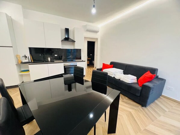 A modern living space with a dining area, kitchen, and a black sofa with red cushions. - New Listing (Sanremo)